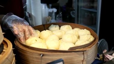 Buharda pişmiş bir çöreği (Salapao) bambu buharlı bir buharlı gemiden kaldıran bir satıcının yakın çekimi. Dramatik yükselen buhar tazeliği ve otantik Asya sokak yiyecekleri ritüelini vurguluyor.
