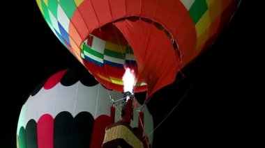Yoğun bir propan yakıcı ateşle aydınlatılan sıcak hava balonlarının güçlü gece görüntüleri. Parlak alev balon gölgeliğini aydınlatarak festival, seyahat ve macera içeriği için ideal dramatik ve enerjik bir atmosfer yaratıyor..
