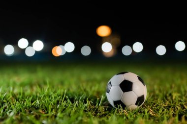 Gece çimlerin üzerinde futbol topu stadyum ışıkları ve fotokopi alanı. Uluslararası turnuva markalaşması, spor haberleri medyası ve futbol taraftarları için maç günü tanıtım materyalleri için yüksek kaliteli arka plan.