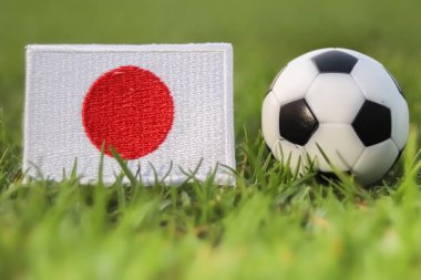 Japon ulusal bayrağı ve futbol topu stadyum çimlerinde akşam ışıklarıyla. Bu sembolik imaj, Asya futbolunun küresel turnuvalardaki tutkusunu ve gururunu temsil ediyor. Spor medyası ve marka projeleri için mükemmel..