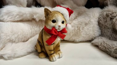 Kış dekoru, şapkalı altın bir kedi ve kırmızı bir fiyonk, açık kürk arka plan, kart ve tatil konsepti.