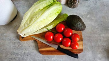 Evde düzgün beslenme, taze sebze ve avokado, tahta tahtada siyah saplı bir bıçakla taze salata. Biber baharatları ve peçeteler mutfak masasında. Mutfak içi, yemek pişirme. 