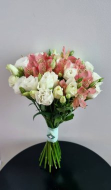 Beyaz ve pembe çiçeklerin yer aldığı düğün buketi, öncelikli olarak östoma, alstromeria, pembe çiçeklerle aksanlı. Dantele sarılmış, sapları dekoratif bir yayla sabitlenmiş..