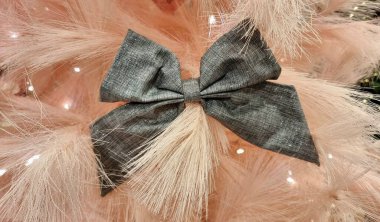 Pembe yapay iğnelerden yapılmış bir Noel ağacı parlak çelenklerle süslenir ve koyu gri fiyonklarla vurgulanır. Fiyonklar düzgün bağlanmış ve yumuşak dokularla çelişiyor.