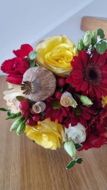 Tanınmış Gerbera papatyaları ve gülleri de içeren kırmızı ve sarı çiçeklerin çarpıcı bir kombinasyonunun yer aldığı renkli bir düğün buketi. Anlaşmada yeşil yapraklar ve küçük kırmızı böğürtlenler var.