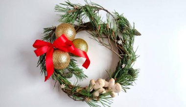 Noel 'in doğal çam dallarının etrafında altın toplar, kırmızı fiyonk, ahşap kar taneleri ve beyaz arka planda çam kozalakları.