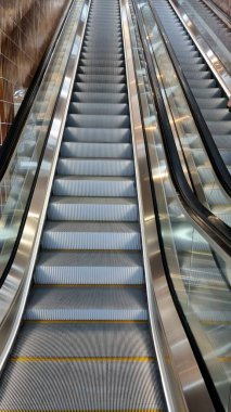 Parlak paslanmaz çelik korkulukların arasından yükselen merdivenleri olan metal yürüyen merdivenler. Her iki taraftaki kahverengi fayans duvarları metalik kaplamayla tezat oluşturarak modern endüstriyel estetiği güçlendiriyor.