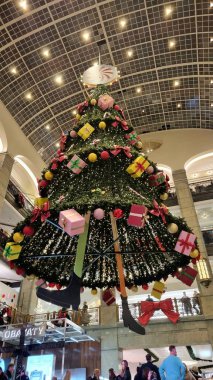 Stockholm, İsveç, 12.20.2025. İsveç 'in Stockholm kentindeki NK alışveriş merkezinde büyük bir Noel ağacı asılı duruyor. Ağaç renkli ışıklar, süsler ve paketlenmiş hediye kutularıyla süslenmiş.