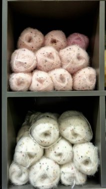 Yün ipliğinden dikiş işi, beyaz ve pembe pullu ahşap bir rafta zarif paketlenmiş iplik izleri. Yaratıcı alan ve ipliklerden örgü