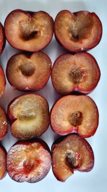 Koyu kırmızı-mor derili yarım erikler, sulu, kehribar renkli etlerini sergilemek için sıra sıra dizilirler. Erikler düzgünce kesilmiş, çukurların kaldırıldığı yerleri gösteriyor..