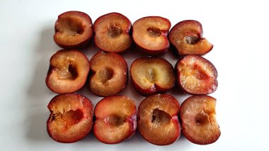 Koyu kırmızı-mor derili yarım erikler düzenli olarak sıralanır. Sulu, kehribar renkli derileri canlı deriyle çelişiyor. Ortadaki taş oyukları ortaya çıkıyor.