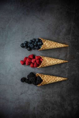 Koyu taştan arka planda waffle külahında taze böğürtlen, üst manzara. Sağlıklı yiyecekler ve çöl kavramı.