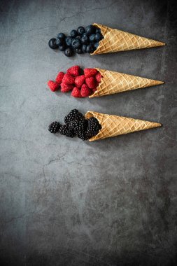 Koyu taştan arka planda waffle külahında taze böğürtlen, üst manzara. Sağlıklı yiyecekler ve çöl kavramı. Boşluğu kopyala.