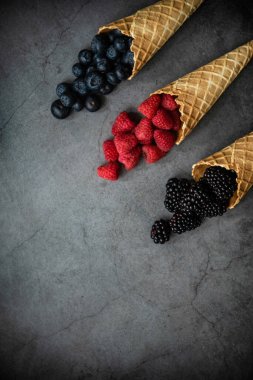 Koyu taştan arka planda waffle külahında taze böğürtlen, üst manzara. Sağlıklı yiyecekler ve çöl kavramı. Boşluğu kopyala.