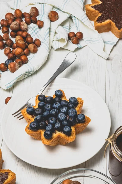 Yıldız şeklinde pandoro panettone üzerine yayılmış ev yapımı fındıklı çikolatalı tereyağı. Beyaz ahşap arka planda yaban mersini, fındıklı, koyu çikolatalı. Noel yemeği konsepti.