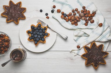 Kavanozda ev yapımı fındıklı çikolatalı tereyağı ve beyaz ahşap arka planda yaban mersini, fındıklı, koyu çikolatalı yıldız şeklinde pandoro panettone parçalarına yayılmış. Üst Manzara. Noel yemeği konsepti.
