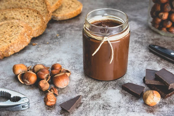 Homemade hazelnut chocolate butter, hazelnut, dark chocolate, on black stone background. The concept of cooking chocolate and nut paste.