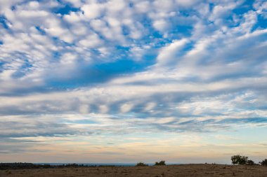 A vast, arid landscape stretches beneath a blue sky streaked with scattered clouds