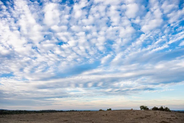 A vast, arid landscape stretches beneath a blue sky streaked with scattered clouds