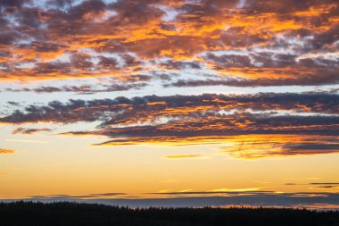 Kızgın bulutlar, gün batımında dramatik bir gökyüzünde kıvrılır, derin maviler, morlar, portakallar ve altın sarılarını harmanlayarak nefes kesici bir görüntüde.