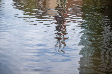 Binaların ve figürlerin çarpık yansımaları su üzerinde dalgalanarak soyut, resmedilmiş kentsel bir serap yaratıyor..