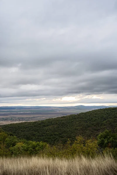 Güneş ışığı, yuvarlanan tepeler ve kuru otlar üzerinde yoğun gri bulutları yararak kasvetli bir sonbahar gökyüzünün altında geniş bir ovayı ortaya çıkarıyor..