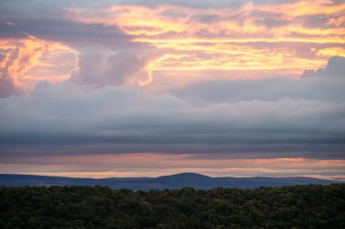 Pembe, turuncu ve mor renkli bulutlar gölgeli tepeler ve ormanlar üzerinde sürükleniyor. Gün doğumunda ya da günbatımında dingin bir parıltı bırakıyorlar..