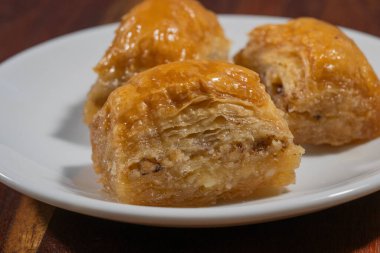 Üç altın, şurup kaplı baklava parçası davetkar bir şekilde beyaz bir tabakta oturuyor.,