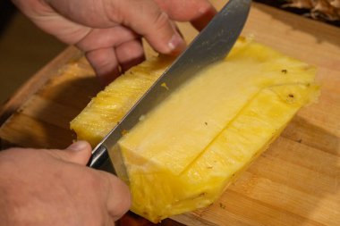 Bir el dikkatle bir ananas dilimini ahşap bir tahtada soyar.