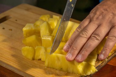 Yeni soyulmuş bir ananas, tahta bir kesme tahtasının üzerinde parçalara ayrılıyor.