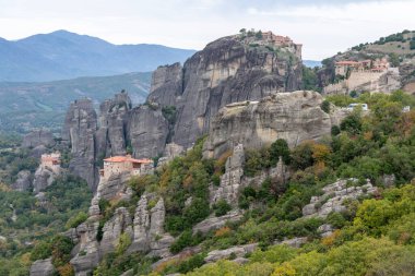 Manastırlar, yemyeşil ve uzak dağ sırtlarıyla çevrili, Meteoraların tepesinde yükselen kaya sütunları..