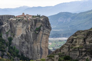 Kırmızı kiremitli çatıları olan bir manastır Meteora 'daki kumtaşı uçurumunun tepesinde duruyor.