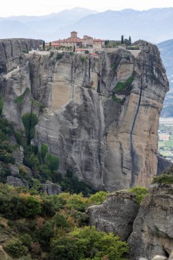 Kırmızı kiremitli çatıları olan bir manastır Meteora 'daki kumtaşı uçurumunun tepesinde duruyor.