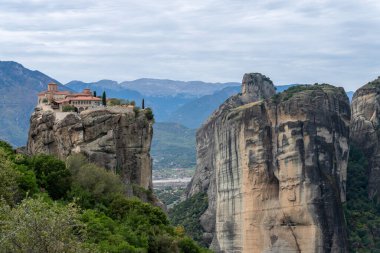 Kırmızı kiremitli çatıları olan bir manastır Meteora 'daki kumtaşı uçurumunun tepesinde duruyor.