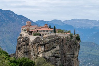 Kırmızı kiremitli çatıları olan bir manastır Meteora 'daki kumtaşı uçurumunun tepesinde duruyor.