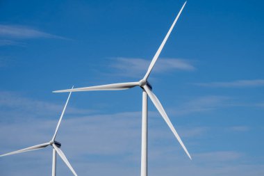 Temiz bir gökyüzü altında, temiz enerji ve modern sürdürülebilirliği sembolize eden iki rüzgar türbini yükselir..