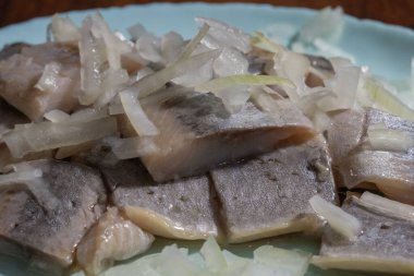 Dilimlenmiş soğanla kaplı turşulu ringa balıkları açık mavi bir tabakta servis edilir..