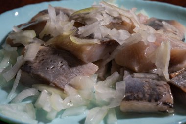 Dilimlenmiş soğanla kaplı turşulu ringa balıkları açık mavi bir tabakta servis edilir..