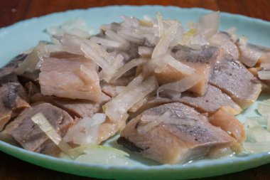 Dilimlenmiş soğanla kaplı turşulu ringa balıkları açık mavi bir tabakta servis edilir..