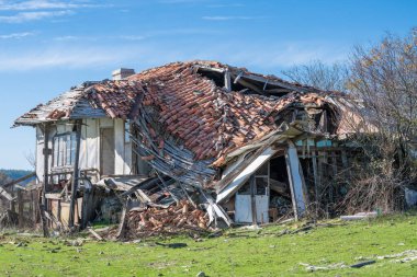 Ağır hasarlı ve kısmen çökmüş çatı kiremitleri ve yıkılan duvarlarla terk edilmiş bir ev..