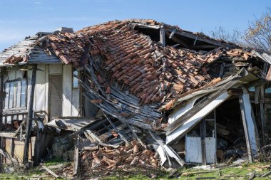 Ağır hasarlı ve kısmen çökmüş çatı kiremitleri ve yıkılan duvarlarla terk edilmiş bir ev..