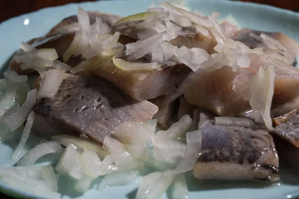 Dilimlenmiş soğanla kaplı turşulu ringa balıkları açık mavi bir tabakta servis edilir..