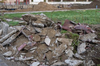 Kırık beton, metal çubuklar ve kırmızı kiremitlerle dolu bir inşaat enkazı çimenli bir arazinin yakınında duruyor..