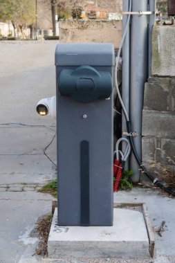 Otomatik erişim için güvenlik kamerası ve elektrik kablolarıyla donatılmış modern bir park kapısı sistemi var.