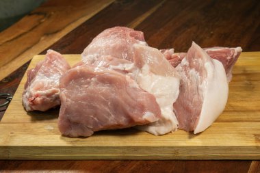 Yeni kesilmiş çiğ domuz eti ve görünür mermer mutfak ortamında ahşap bir kesme tahtasının üzerinde dinleniyor..