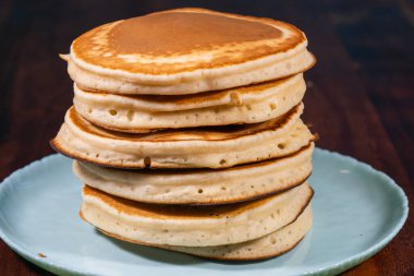 Altı altın-kahverengi, tüylü krep yığını açık mavi bir plaka ile koyu bir arka plan üzerine kuruludur.