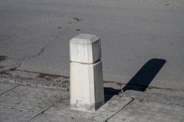 Çatlamış bir şehir yolunun kenarındaki kaldırımda beton bir kazık uzun bir gölge bırakıyor..