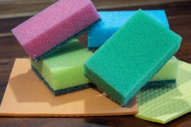 Renkli temizlik süngerleri ve giysiler ahşap bir yüzeye yerleştirilmiş, ev kullanımına hazır..