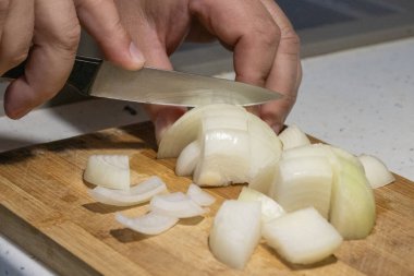 Birisi beyaz soğanı mutfak bıçağı kullanarak tahta bir kesme tahtasının üzerinde orta parçalara ayırıyor..