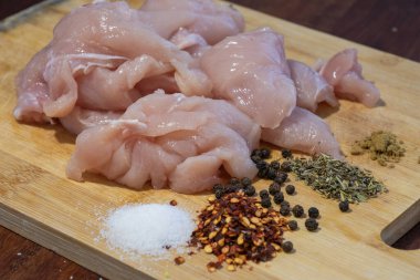  Çiğ tavuk parçaları ve tuz, biber taneleri, biber, kurutulmuş otlar ve ahşap kesim tahtasındaki yer baharatı gibi çeşitli baharatlar..